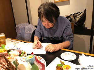 原稿チェックとサマーセミナー事務局Tシャツの一言を書く向山先生。 どこでも仕事をする。（させている?!）